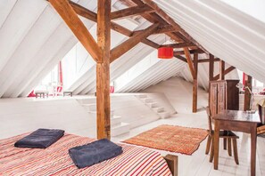 Ein Schlafzimmer im Dachgeschoss mit schrägen Wänden, Holzbalken, einem kleinen Tisch und zwei Betten mit Kissen.