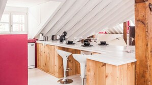Een moderne keuken met een wit aanrecht, houten kastjes en twee witte barkrukken.