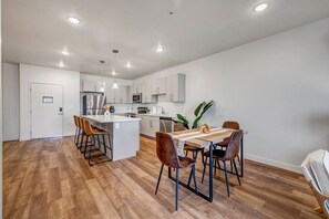Uma cozinha moderna com armários brancos, uma ilha central e uma área de refeições com mesa e cadeiras de madeira.