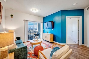 Een woonkamer met een groot raam, een flatscreen-televisie en een schuifpui naar een balkon.