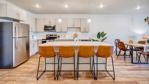 A modern kitchen with stainless steel appliances, a central island with bar stools, and pendant lighting. - Bold Boho Themed 2bd 2ba (Draper)