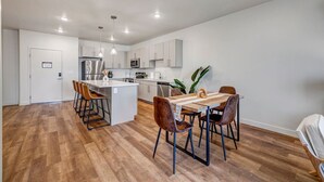A modern kitchen with white cabinets, a central island, and a dining area with a wooden table and chairs. - Bold Boho Themed 2bd 2ba (Draper)