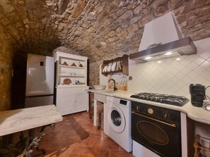 Eine kleine Küche mit Steinwand, integriertem Waschmaschine, Herd und weißem Kühlschrank.