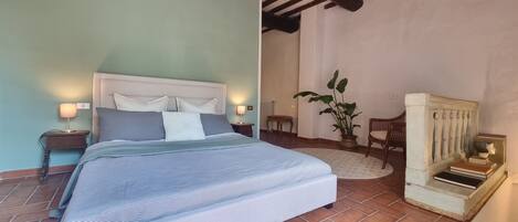 A bedroom with a bed, bedside lamps, a potted plant, a chair, and a small table.