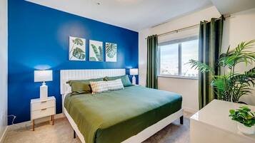 A bedroom with a bed, bedside tables, a window with curtains, and a view of the city.