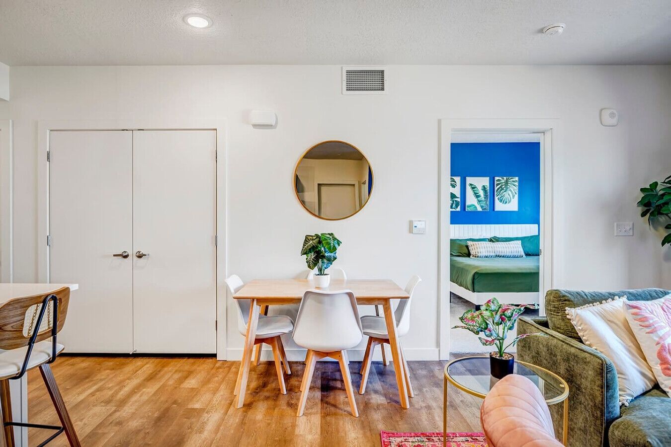 A compact living space with a dining area, a round mirror, a sofa, and a bed with a blue accent wall.