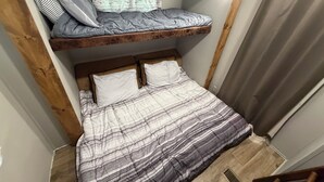 Une chambre avec un lit superposé, un lit en bas, une fenêtre avec des rideaux et une tête de lit en bois.