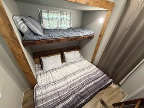 Ein Zimmer mit Etagenbett, einem unterem Bett, einem Fenster mit Vorhängen und einem hölzernen Kopfteil.