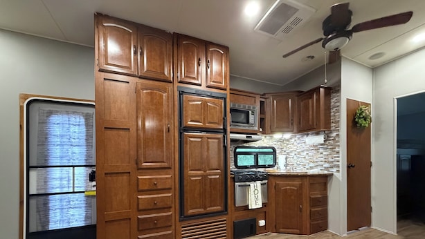 Une cuisine avec des meubles en bois, un four à micro-ondes, une cuisinière et un ventilateur de plafond.