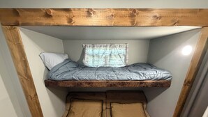 Un lit superposé avec une tête de lit en bois, une fenêtre ornée d’un rideau à rayures et deux oreillers sur le lit du bas.