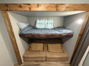 Ein Stockbett mit Holz-Kopfteil, ein Fenster mit gestreifter Gardine und zwei Kissen auf der unteren Schlafstelle.