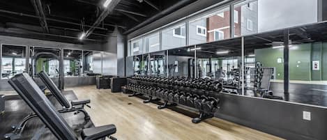 Une salle de sport équipée de matériel de musculation, de miroirs et dotée d’un plancher en bois.