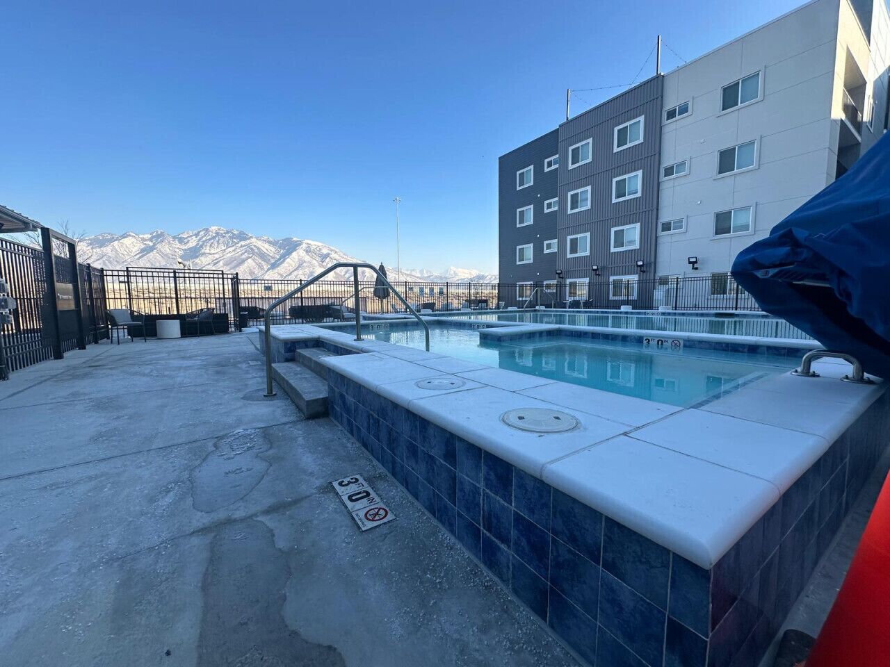 A rooftop pool with a view of mountains, a building with multiple windows, and a blue-tiled edge.