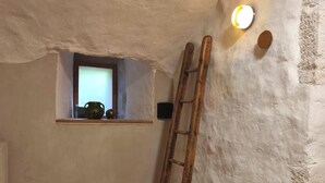 Quarto rústico com parede de pedra, escada de madeira, uma pequena janela e uma prateleira com um vaso.