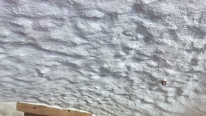 Quarto com cama, porta de madeira, luminária e uma mesa pequena.
