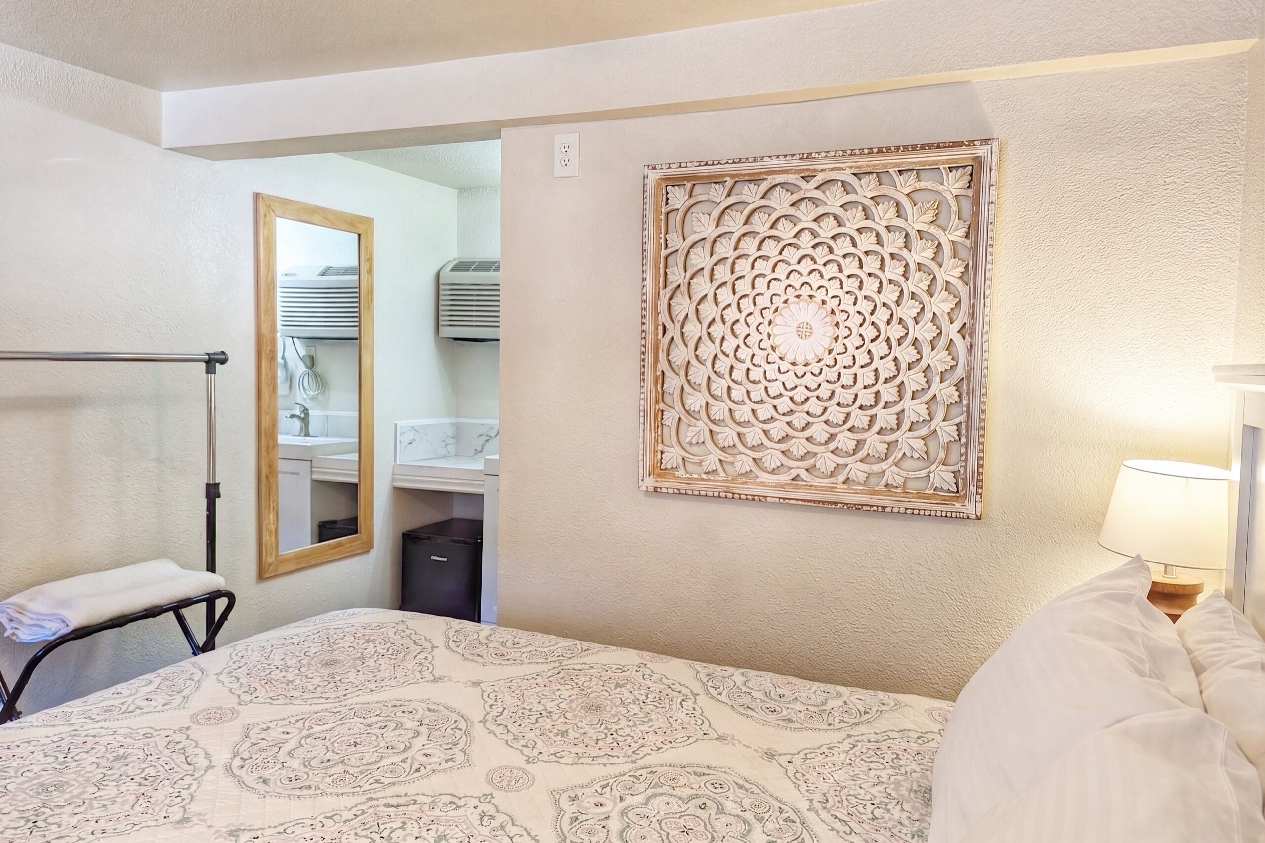 Ett hotellrum med en säng, en spegel, en dekorativ väggpanel och en sänglampa.