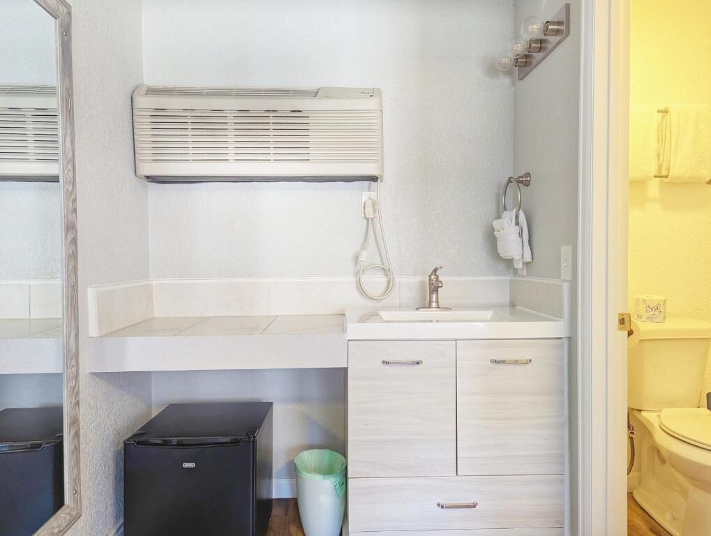 A bathroom with a white sink, mirror, and towel rack. There is a white cabinet with drawers and a trash bin.