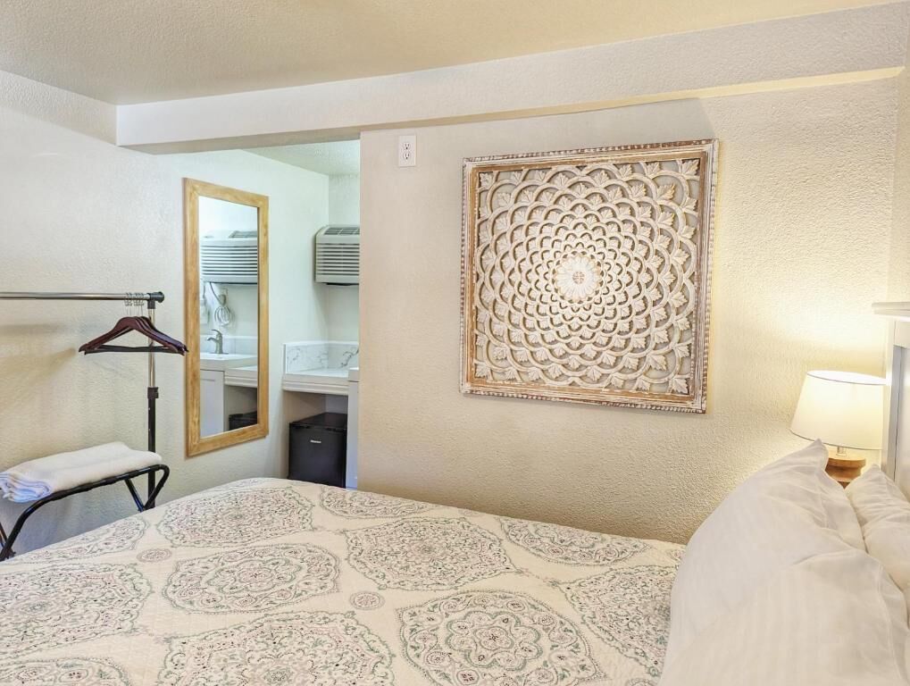 Een hotelkamer met een bed, een handdoekhouder, een spiegel, een decoratief wandpaneel en een bedlamp.