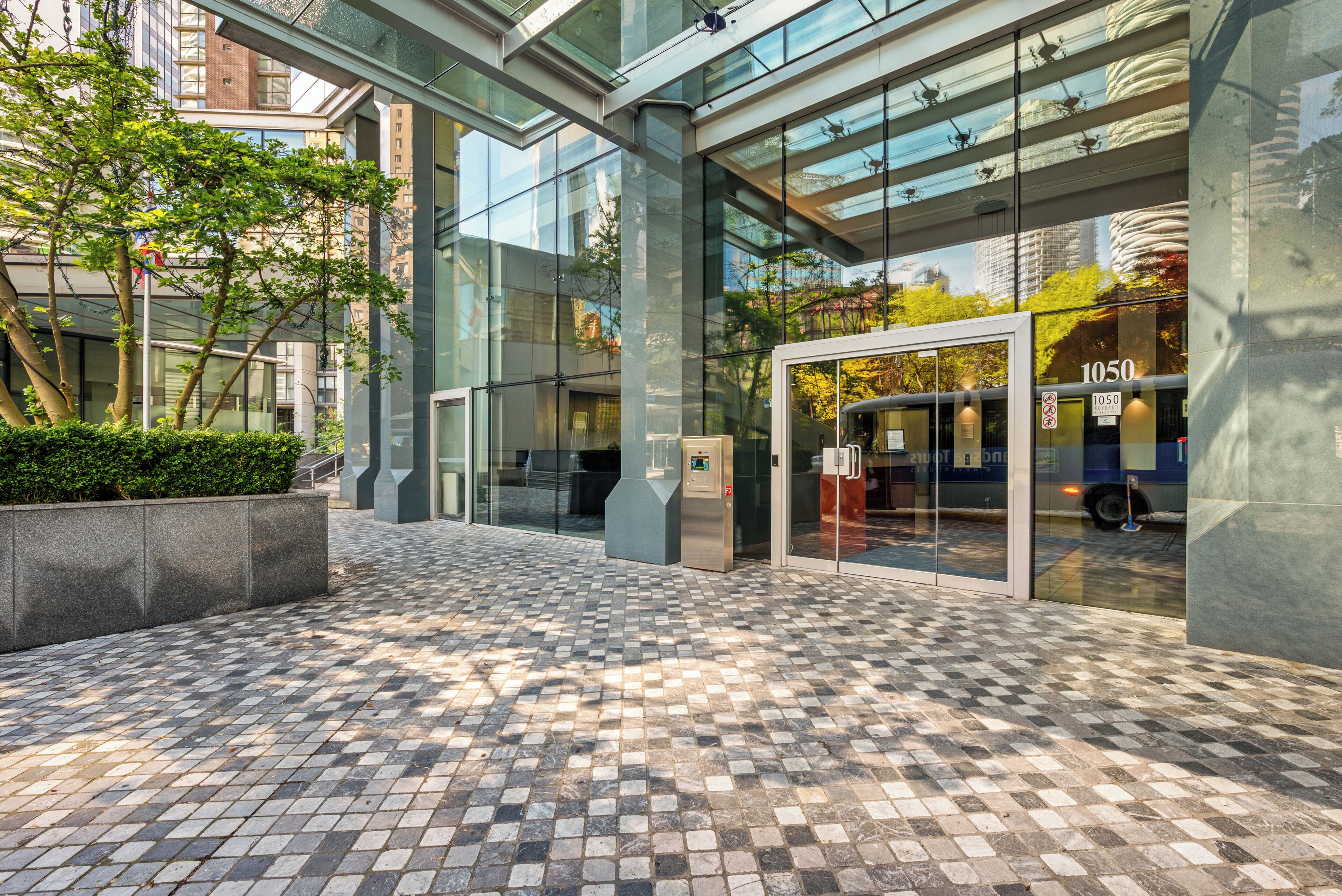 A modern building entrance with glass doors, a checkered floor, and a clear view of the sky.