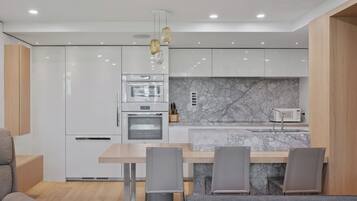 A modern kitchen with white cabinetry, a marble backsplash, and a dining area with grey chairs.