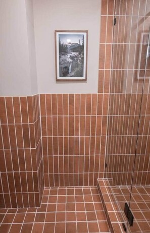 Une salle de bain avec des murs recouverts de carreaux marron et un tableau encadré représentant un paysage.