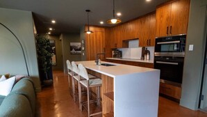 A modern kitchen with wooden cabinets, a white island, and a built-in oven. - Fernwood - Views ULTRA Comfort A+ Design 1335sf 4b (Canmore)