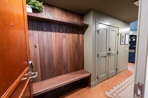 Un pasillo con un banco de madera, un perchero y un juego de dos puertas grises.