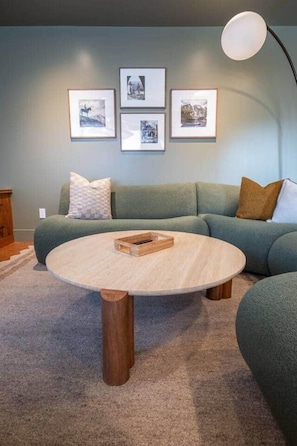 Ein Wohnzimmer mit einem grünen Sofa, einem runden Couchtisch und gerahmten Bildern an der Wand.