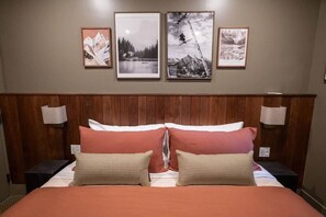 Een hotelkamer met een houten hoofdeinde, een bed met twee kussens en drie ingelijste foto's aan de muur.