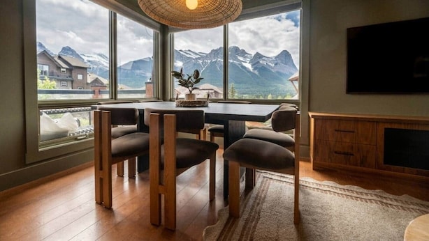 A dining area with a view of mountains, a woven light fixture, and a flat-screen TV. - Fernwood - Views ULTRA Comfort A+ Design 1335sf 4b (Canmore)