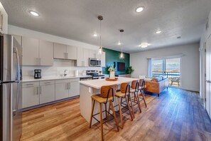 A modern kitchen with a central island, bar stools, a dining area, and a large window with a view.