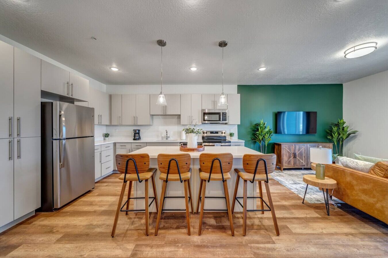 A modern kitchen with a central island, stainless steel appliances, and wooden chairs.