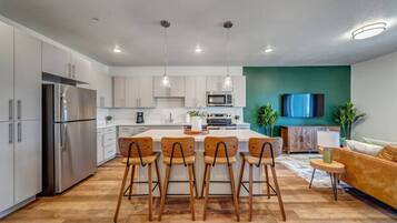 A modern kitchen with a central island, stainless steel appliances, and wooden chairs.