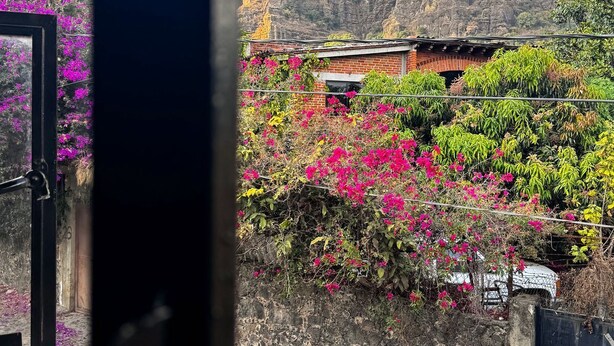A view through a window of a building with a stone wall, a brick structure, and a mountain in the background. - Umbral (Tepoztlan)