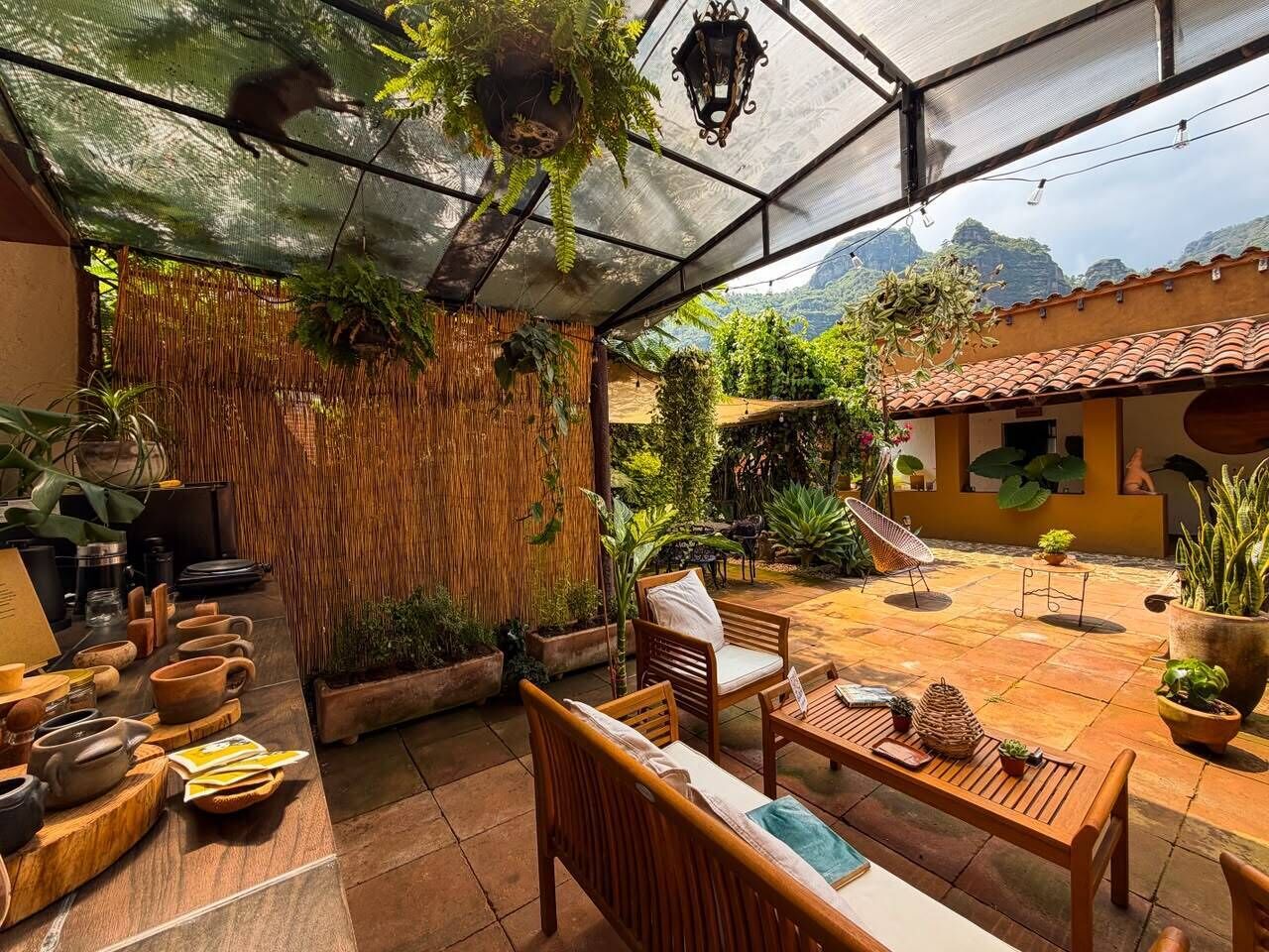 Un patio techado al aire libre con mobiliario de madera, plantas en macetas y vistas a un paisaje montañoso.
