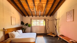 A bedroom with a wooden ceiling, a bed, a window, a plant, and a bench. - Umbral (Tepoztlan)