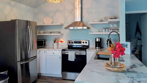Una cocina moderna con un refrigerador de acero inoxidable, un microondas, un horno y un lavamanos. Hay una lámpara colgante sobre la encimera.