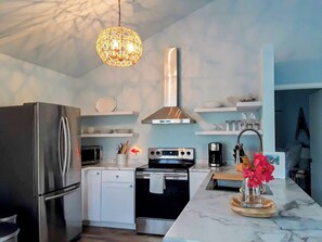 A modern kitchen with a stainless steel refrigerator, a microwave, an oven, and a sink. There is a hanging light fixture above the counter. - Waterfront Cottage in the Keys - 2 bed 2 bath, pet friendly (Cudjoe Key)