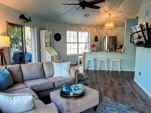 A living room with a sofa, ottoman, and a ceiling fan. - Waterfront Cottage in the Keys - 2 bed 2 bath, pet friendly (Cudjoe Key)