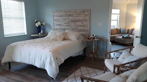 Un dormitorio con cama, mesita de noche, silla y vista a otra habitación.