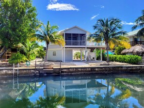 Una casa de dos pisos con balcón, piscina y palmeras.