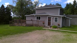 A two-story house with a front porch, a small deck, and a gravel driveway.