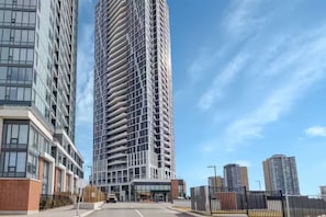 A modern high-rise building with a distinctive curved facade, large windows, and a gated entrance. - Urban Luxury Condo in the heart of Kitchener. (Kitchener)