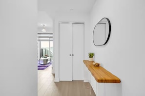 A hallway with a white door, a wooden console table with a plant, and a mirror on the wall. - Urban Luxury Condo in the heart of Kitchene. (Kitchener)