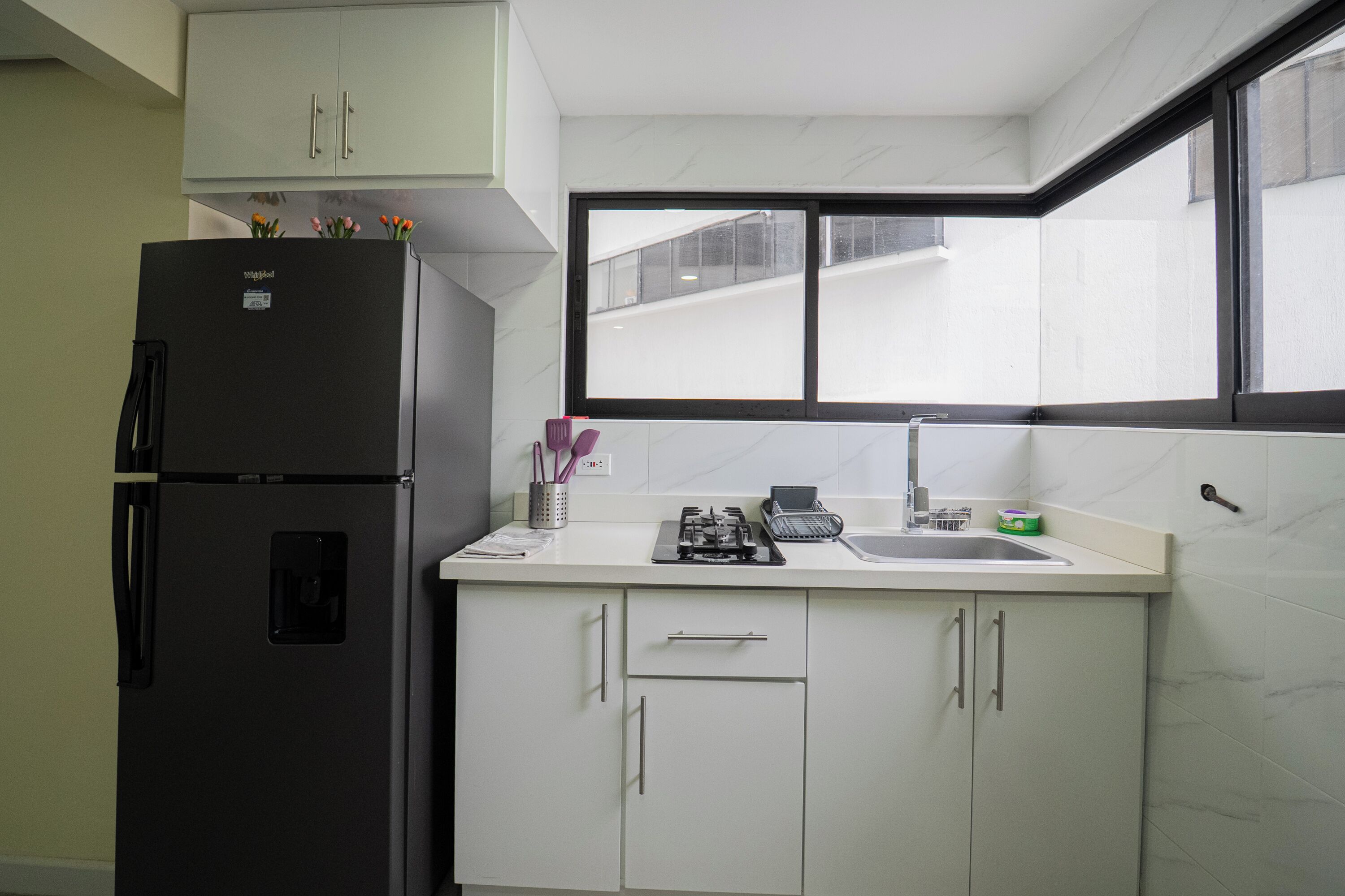A kitchen with a refrigerator, cabinets, a window, and a sink.