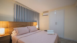 Uma cama bem arrumada com cabeceira, mesa de cabeceira com abajur, guarda-roupa e ar condicionado.