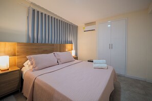 Ein ordentlich bezogenes Bett mit Kopfteil, ein Nachttisch mit Lampe, ein Kleiderschrank und eine Klimaanlage.