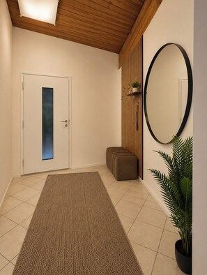 A hallway with a wooden ceiling, a door with a frosted glass panel, a large mirror, a brown rug, and a potted plant.