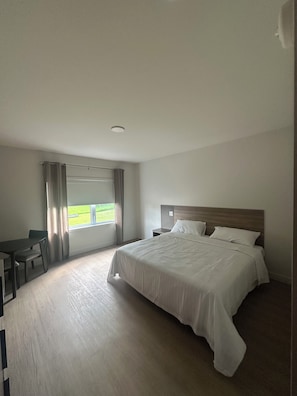 A hotel room with a large bed, a desk, and a window with curtains. - Hotel W Des Cantons (Weedon)