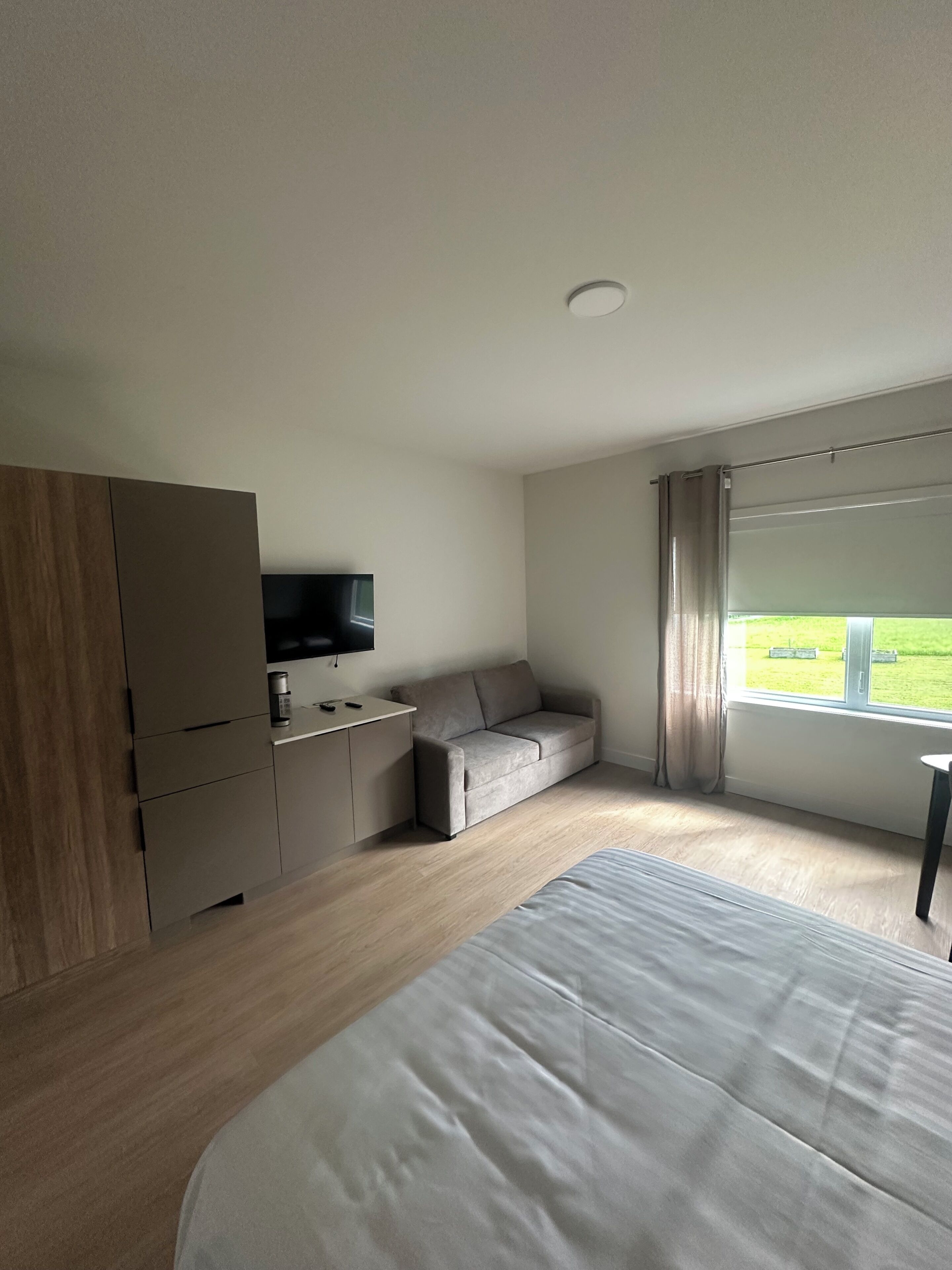Quarto de hotel moderno com cama, sofá, televisão e janela com cortinas.